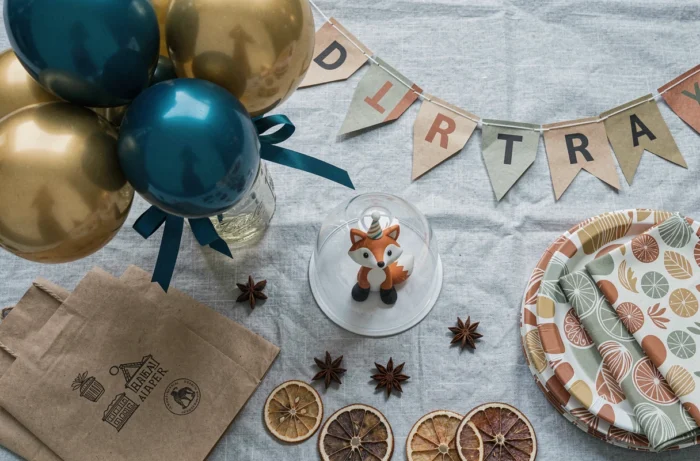Flat lay de fournitures de décoration d'anniversaire originales en kraft, ballons dorés, banderoles et accessoires terracotta et vert sauge